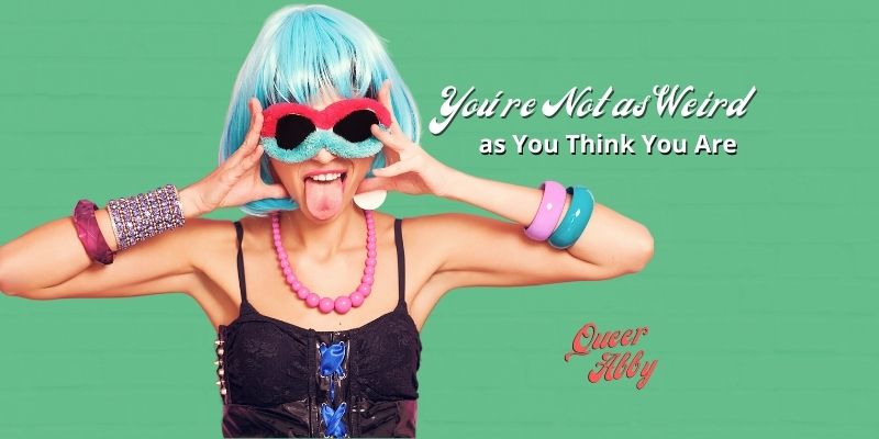 Young white woman wearing a blue wig, fuzzy sunglasses, a black shiny tank top, and chunky pink jewelry is holder her head and sticking out her tongue.